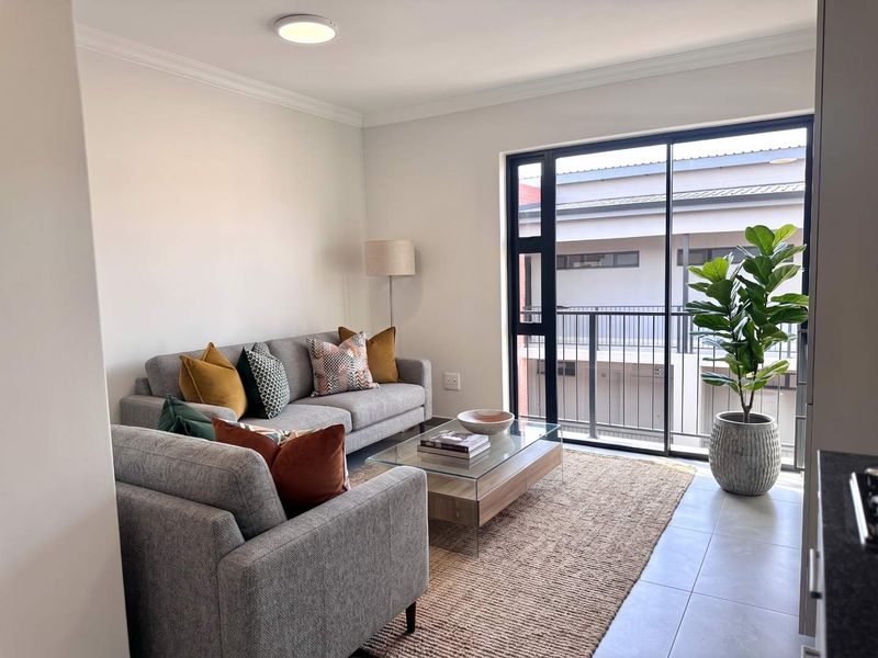 A bright and modern living room featuring tiled flooring and a large sliding glass door that opens onto a balcony.
