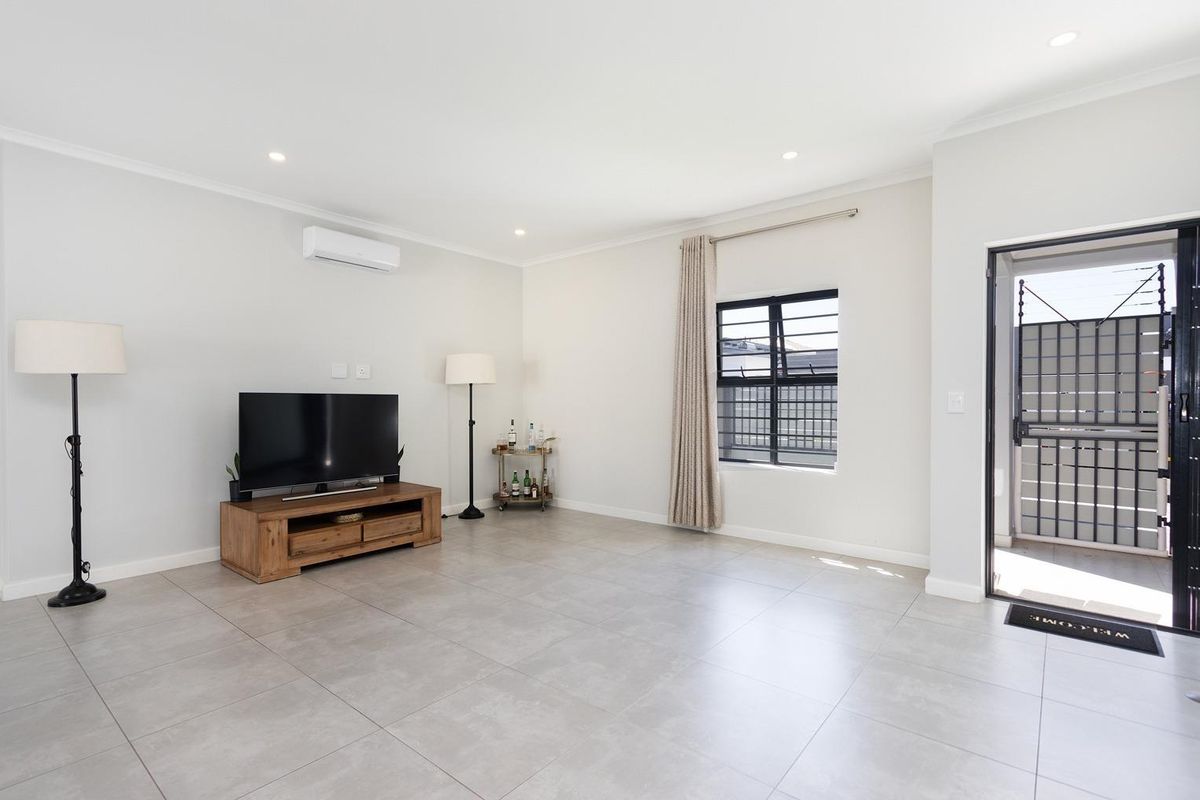 A bright and spacious living room featuring neutral floor tiles, a wall-mounted air conditioning unit, and direct access to an outdoor area.