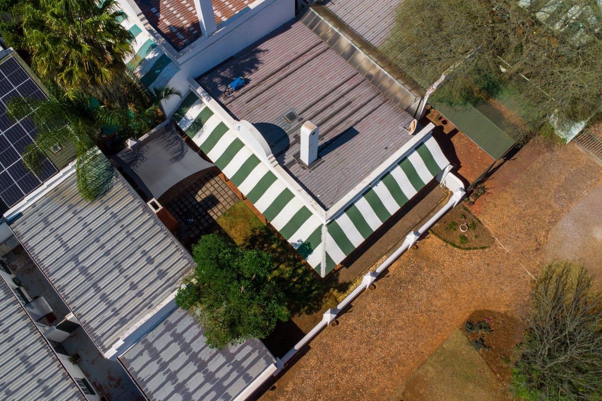 Aerial view of the property showing the roof structure, solar panel installation, paved driveway, and surrounding garden area.