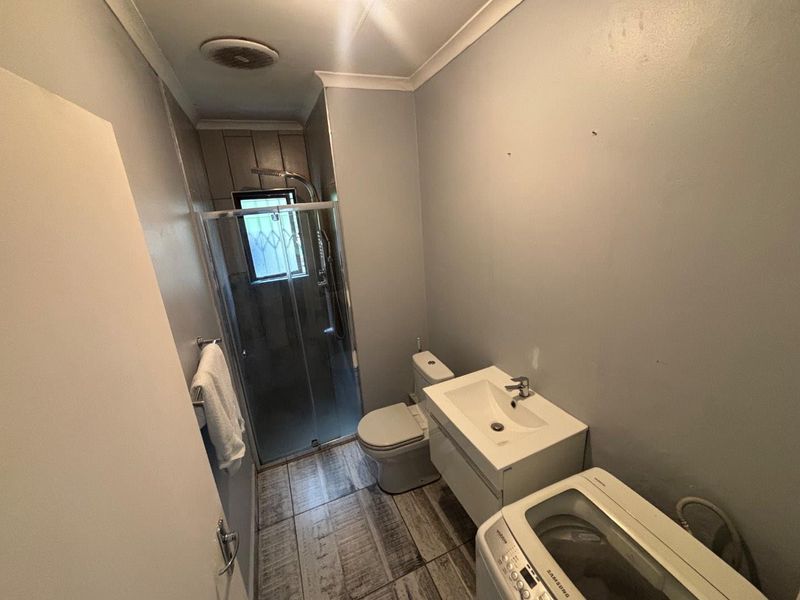 A functional bathroom featuring a shower enclosure, toilet, and vanity basin with tiled flooring and neutral wall finishes.