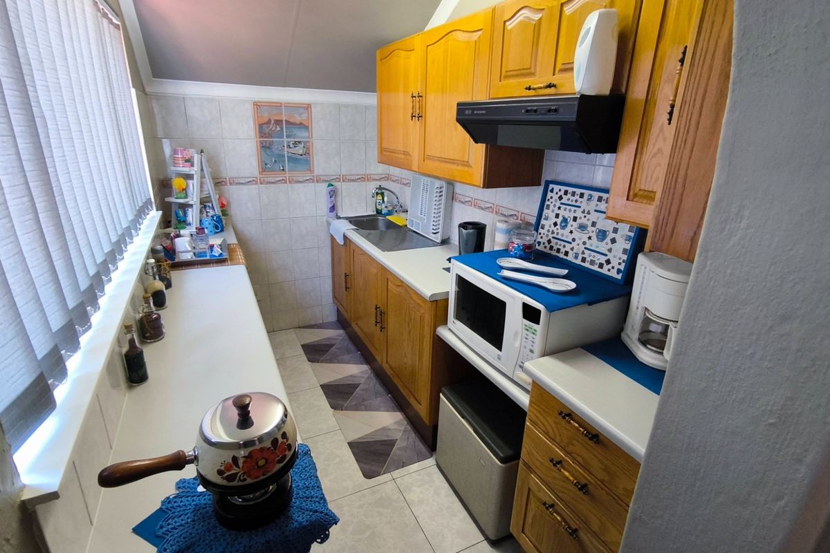 A functional galley-style kitchen featuring wooden cabinetry, tiled backsplash, and ample counter space, offering a practical layout for daily meal preparation.