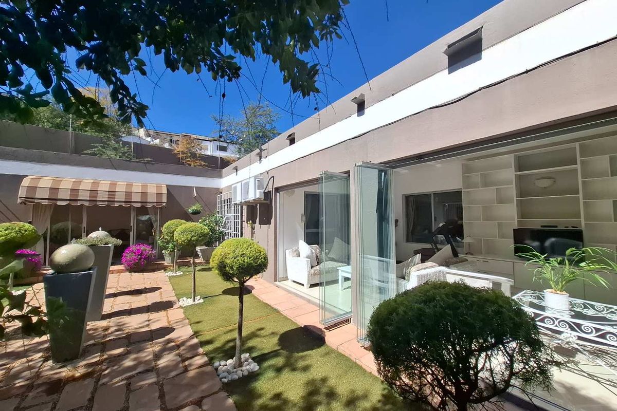 A well-maintained rear courtyard featuring paved walkways, artificial lawn, and seamless indoor-outdoor flow through large glass stacking doors.