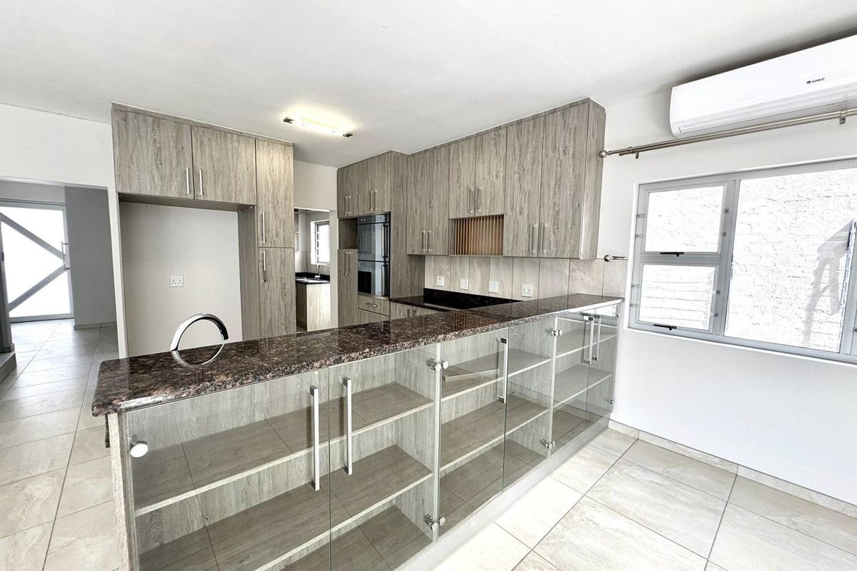 Modern kitchen featuring wood-grain cabinetry, granite countertops, a breakfast bar with glass display shelving, built-in oven, and a wall-mounted air conditioning unit.