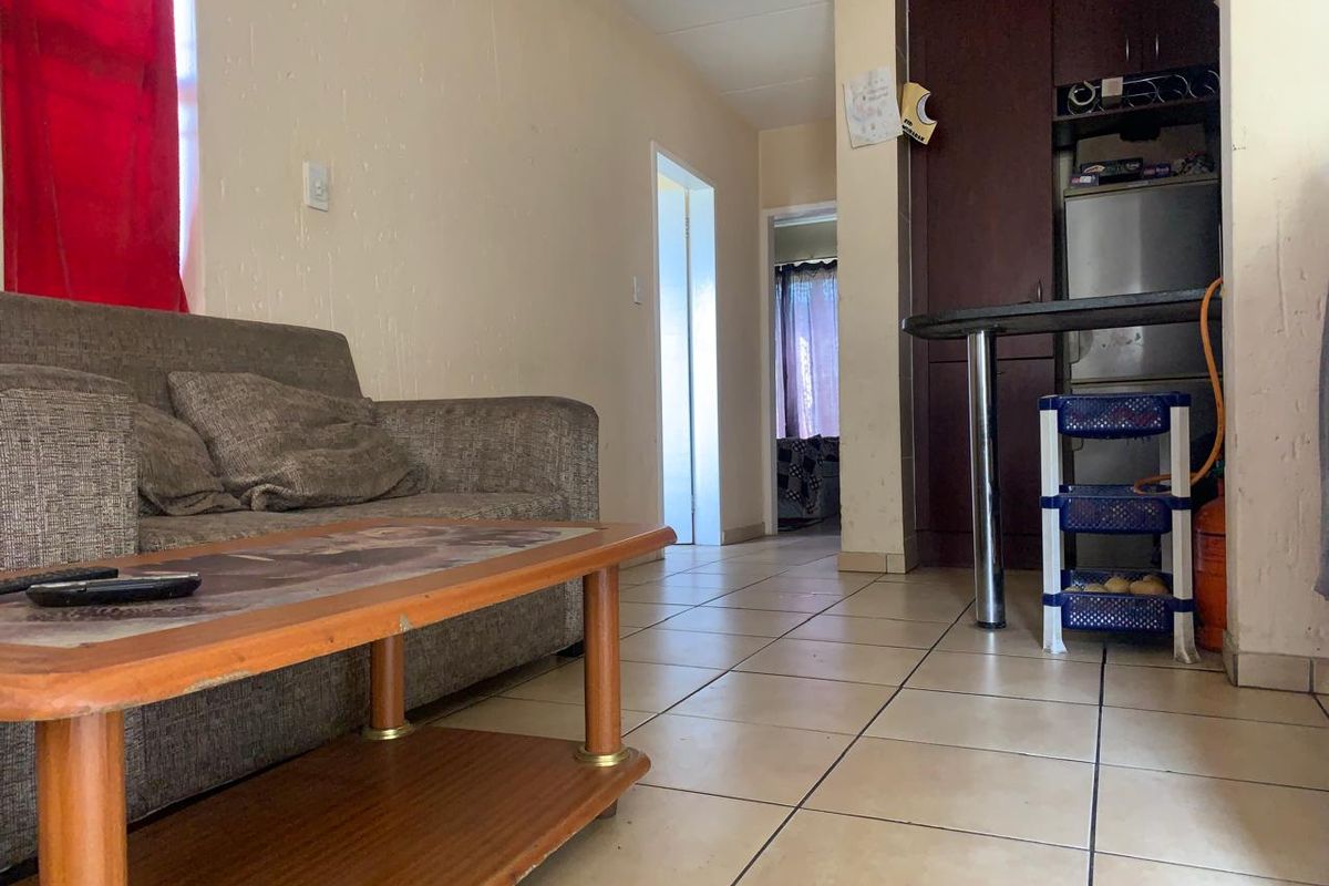 Open plan living area featuring tiled flooring and a compact kitchen with built-in cabinetry and a breakfast bar.