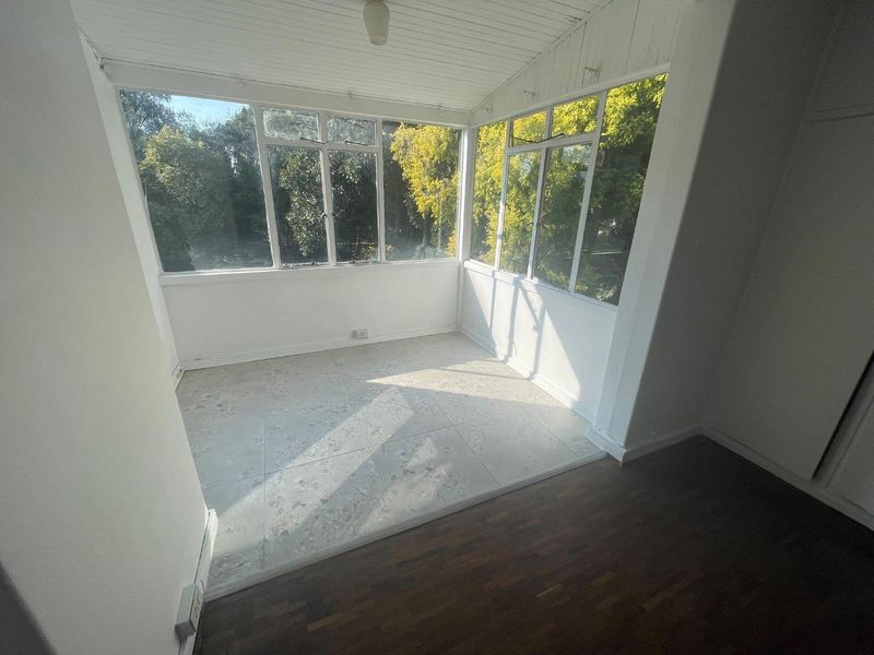 A bright, enclosed sunroom or patio area featuring a mix of tiled and timber flooring with large windows overlooking the garden.