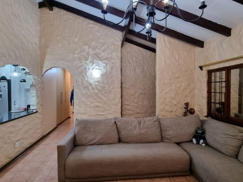 Living room featuring high vaulted ceilings with exposed timber beams, textured plaster walls, and arched architectural openings leading to adjacent spaces.
