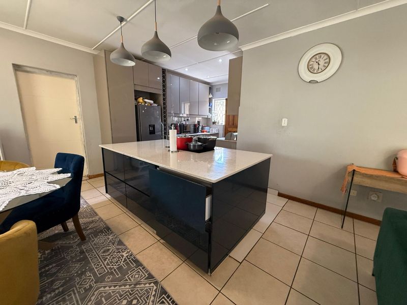 Modern open-plan kitchen featuring a central island with quartz countertops, sleek cabinetry, and ceramic tiled flooring, creating a functional and contemporary living space.