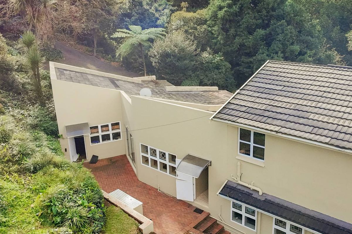 An elevated aerial view of the rear exterior of the house, featuring a paved patio area, tiled roofing, and surrounding established garden greenery.