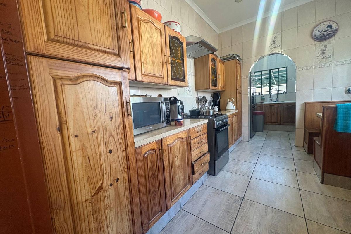 A functional kitchen featuring traditional wooden cabinetry, tiled walls, and flooring, with an arched transition leading to an adjacent scullery or prep area.