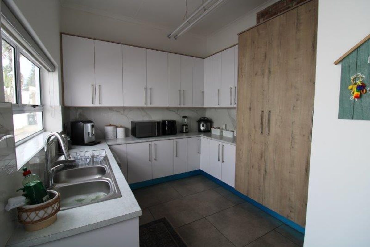 A functional kitchen featuring white and wood-grain cabinetry, stone-look countertops, a double stainless steel sink, and tiled flooring.