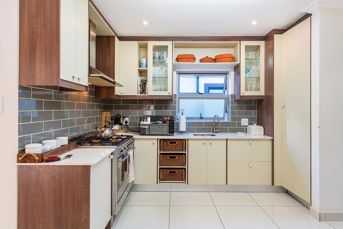 Modern kitchen featuring two-tone cabinetry, subway tile backsplash, stainless steel gas stove with extractor fan, and integrated sink with tiled flooring.