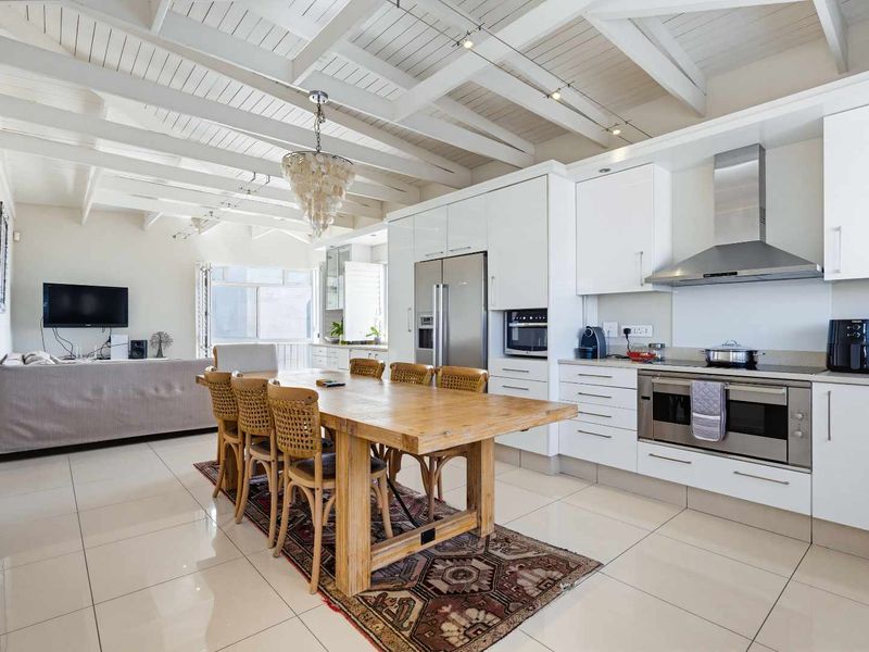 Spacious open-plan living and dining area featuring a modern kitchen with gloss cabinetry, built-in appliances, and a striking exposed beam ceiling.