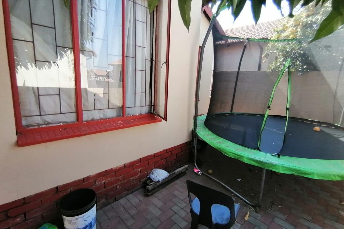 A side exterior area featuring paved flooring, brick base detailing, and red-framed windows.