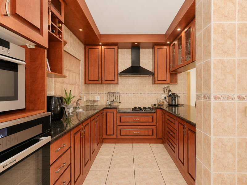 A well-maintained U-shaped kitchen featuring warm wooden cabinetry, granite countertops, a gas hob, extractor fan, and built-in oven with microwave.