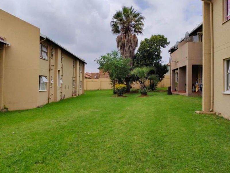 A view of the communal garden area between apartment blocks, featuring well-maintained lawn and perimeter boundary walls.