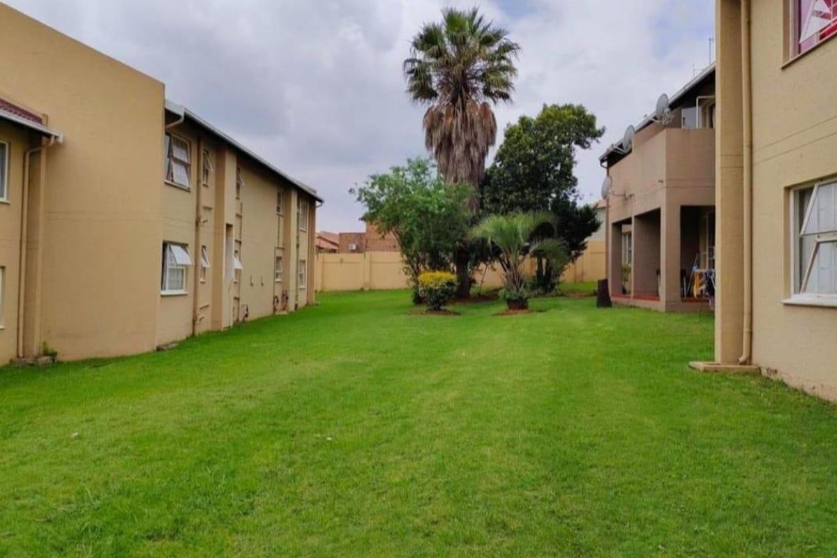 A view of the communal garden area between apartment blocks, featuring well-maintained lawn and perimeter boundary walls.