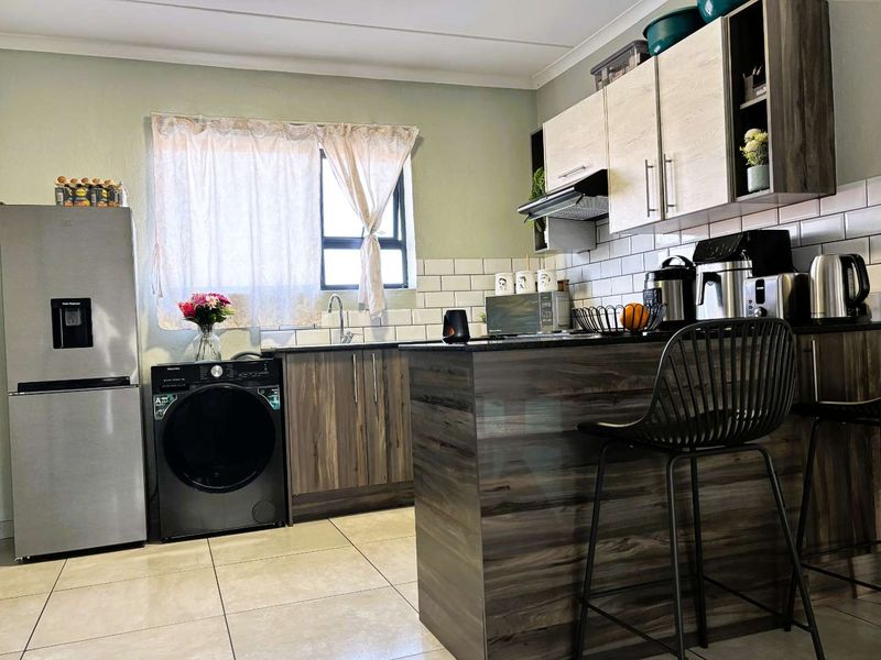 Modern kitchen featuring wood-grain cabinetry, a subway tile backsplash, a functional island, and integrated space for laundry appliances.