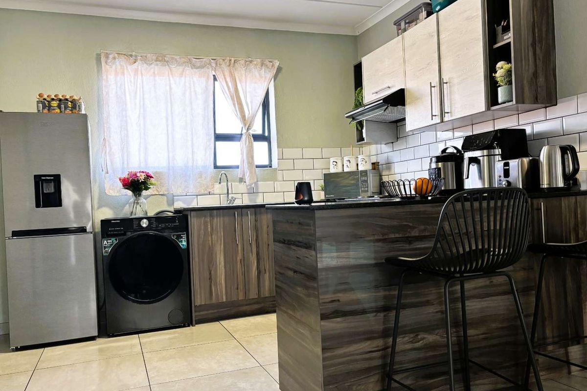 Modern kitchen featuring wood-grain cabinetry, a subway tile backsplash, a functional island, and integrated space for laundry appliances.