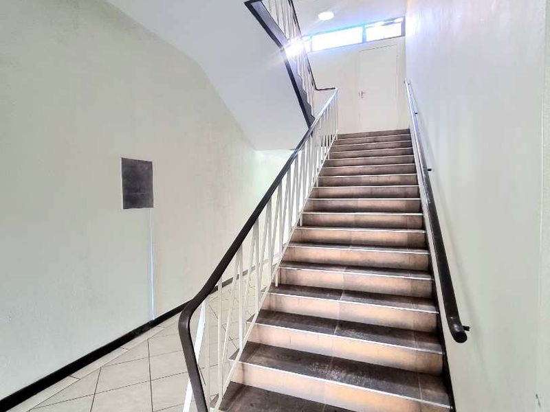 A functional interior stairwell featuring tiled steps, metal handrails, and neutral wall finishes, providing access between levels in the apartment building.