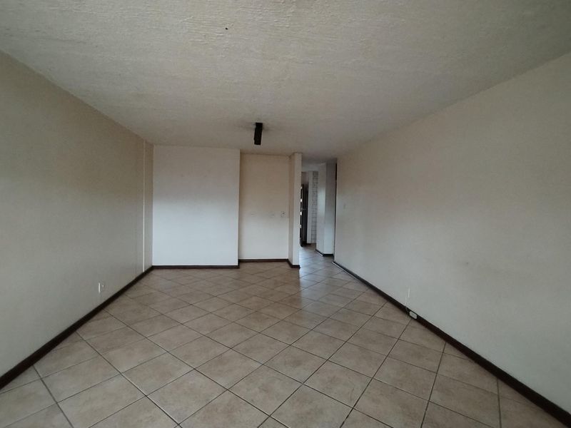 An empty, open-plan living area featuring neutral wall paint and ceramic floor tiles, providing a blank canvas for interior design.