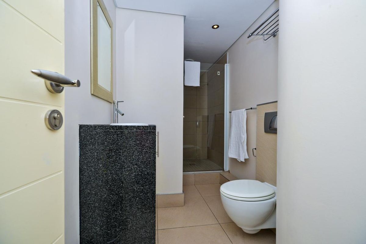 Modern bathroom featuring a wall-mounted toilet, granite-topped vanity with basin, and a glass-enclosed shower with tiled flooring.