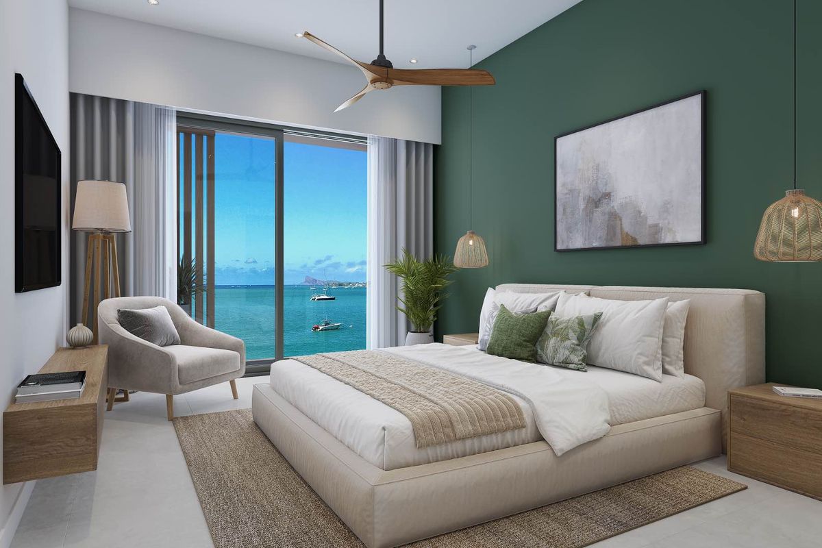 A modern bedroom featuring a green accent wall, ceiling fan, and large sliding glass doors opening to a scenic ocean view.