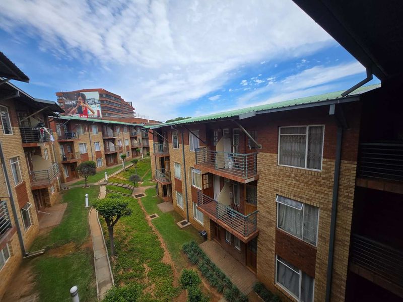 An elevated view of an apartment complex courtyard featuring face brick buildings, metal balcony railings, and a central landscaped garden area.