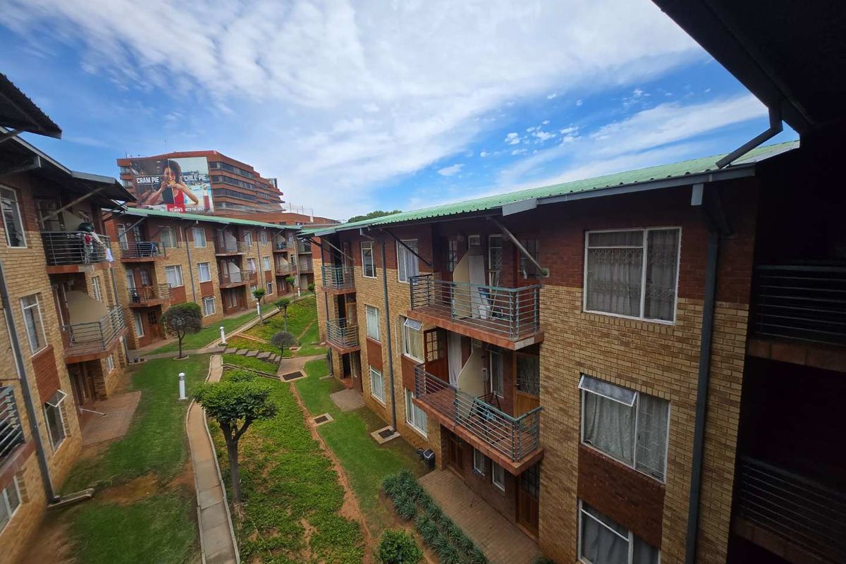 An elevated view of an apartment complex courtyard featuring face brick buildings, metal balcony railings, and a central landscaped garden area.