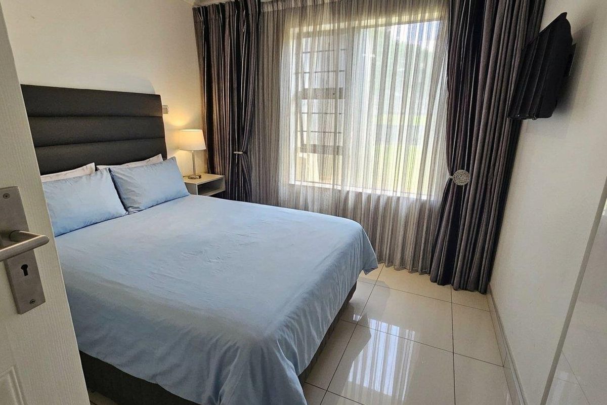 A well-maintained bedroom featuring tiled flooring and a large window with curtains, providing a clean and functional living space.
