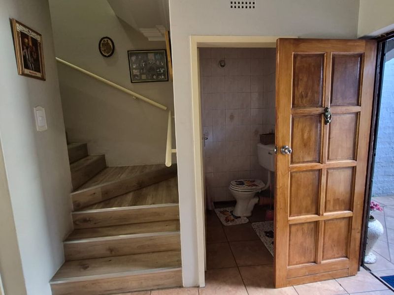 A hallway area featuring a staircase with a handrail, leading to a ground floor bathroom with tiled flooring.