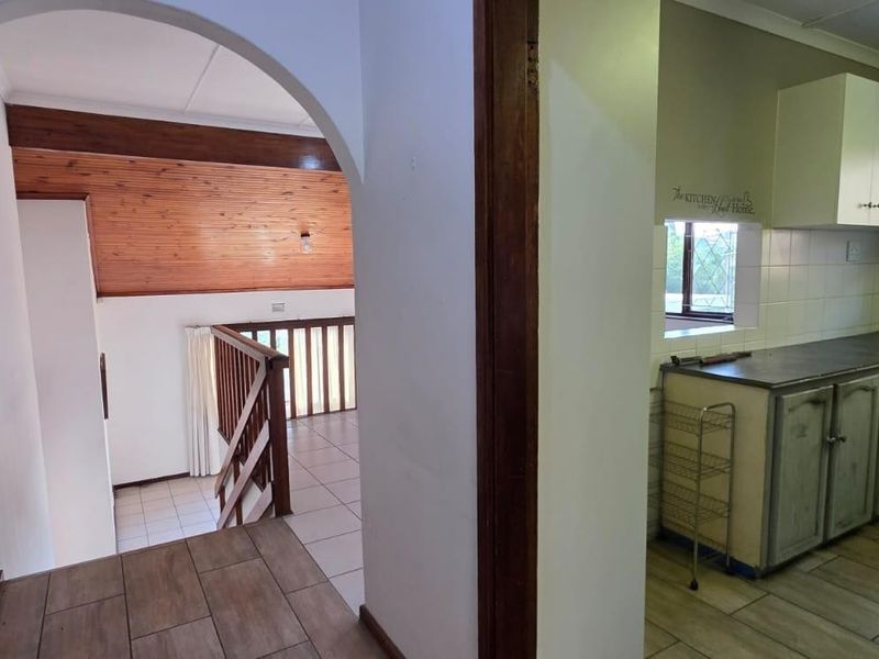 A view from the hallway looking towards a staircase with timber balustrade and an adjacent kitchen area with built-in cabinetry.