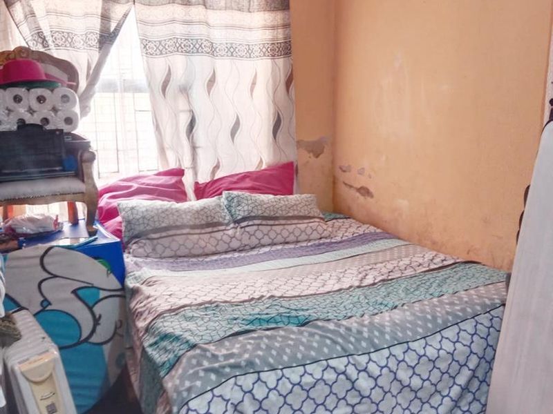 A bedroom featuring a window with curtain rails and visible wall surface damage requiring maintenance and cosmetic repair.