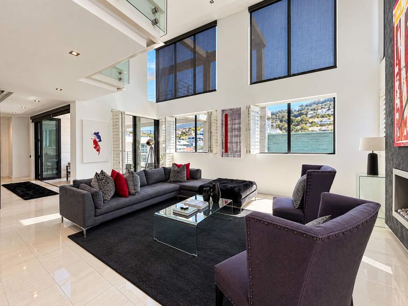 Spacious double-volume living room featuring high ceilings, large windows with roller blinds, tiled flooring, and a modern built-in fireplace.