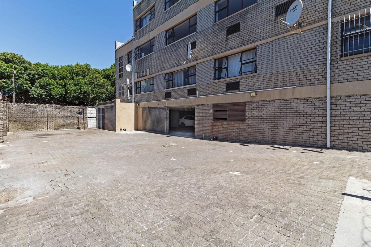 Exterior view of the apartment building featuring a paved parking area, brick facade, and secure gated access to the ground floor parking garage.