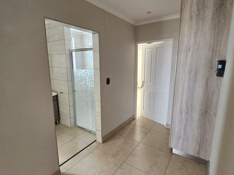 A clean, well-maintained hallway featuring neutral tiled flooring, a built-in wooden cupboard, and direct access to an adjacent bathroom.