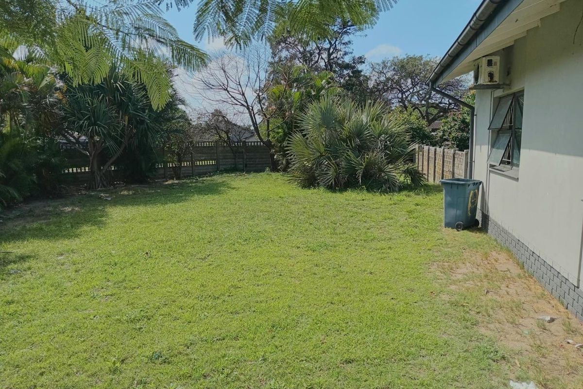 A spacious rear garden featuring a lawn area, perimeter boundary wall, and exterior wall-mounted air conditioning unit.