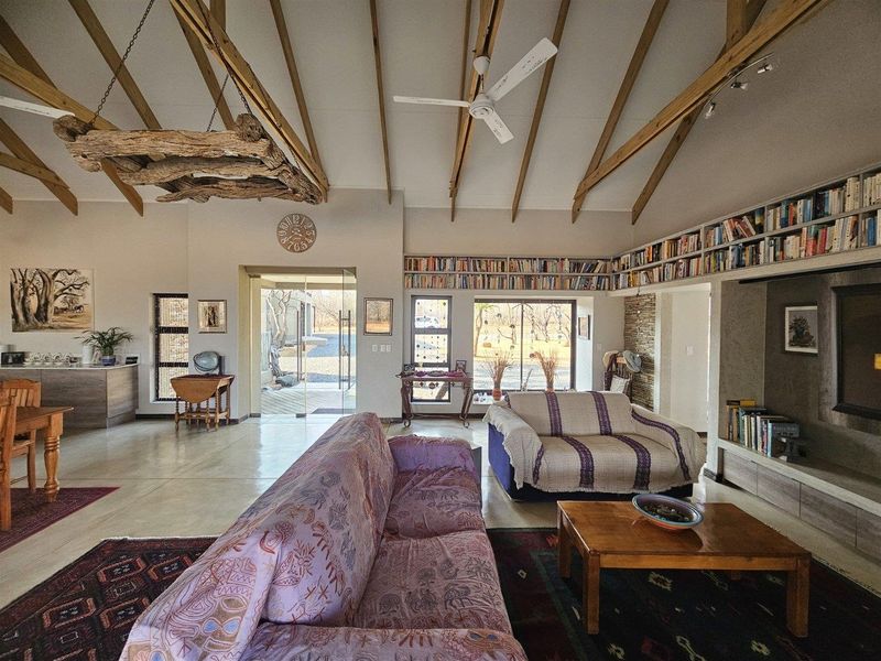 Spacious open-plan living area featuring high vaulted ceilings with exposed timber beams, polished concrete floors, and extensive built-in library shelving.