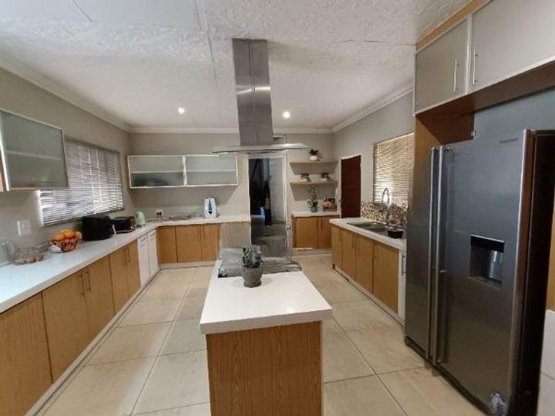 Spacious kitchen featuring a central island, stainless steel extractor fan, ample built-in cabinetry, stone countertops, and tiled flooring.