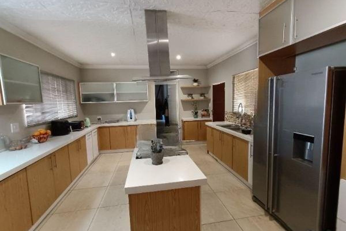 Spacious kitchen featuring a central island, stainless steel extractor fan, ample built-in cabinetry, stone countertops, and tiled flooring.
