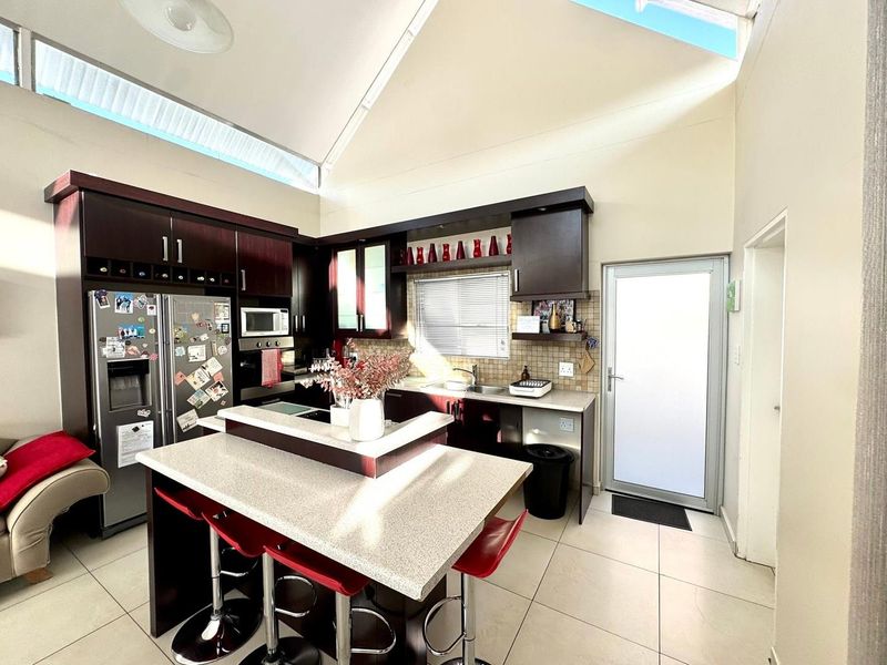 Modern kitchen featuring dark wood cabinetry, stone countertops, a central island, and a high vaulted ceiling with skylights for natural light.