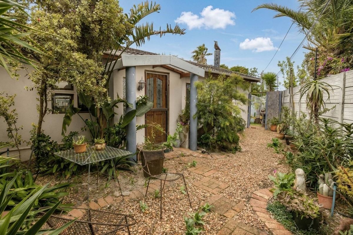 A rear exterior view of the property featuring a gravel garden, brick paved pathway, and a covered entrance porch with structural columns.