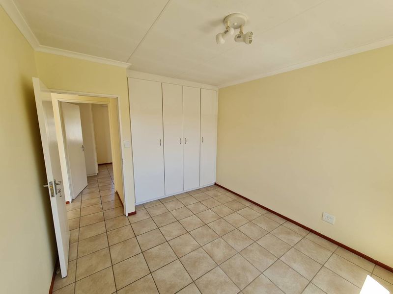 A clean, empty bedroom featuring neutral tiled flooring and ample built-in cupboard storage space.