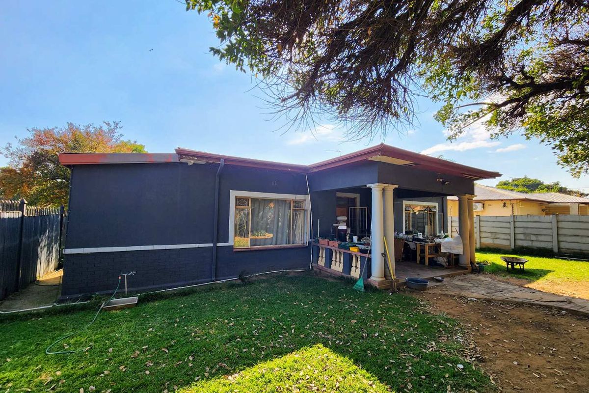 Rear view of the house featuring a covered patio with classic columns, overlooking a private garden area with lawn and perimeter walling.