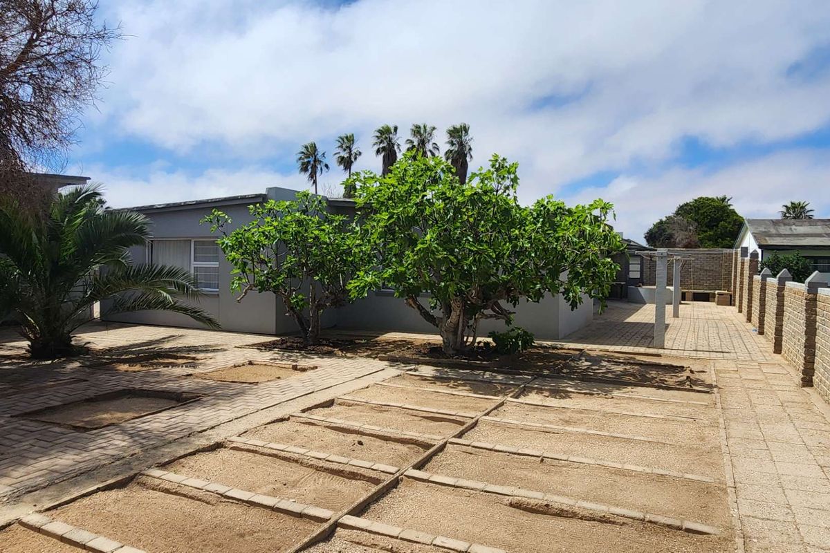 A spacious rear courtyard featuring paved areas, a brick boundary wall, and established trees, offering a functional outdoor space with potential for landscaping improvements.