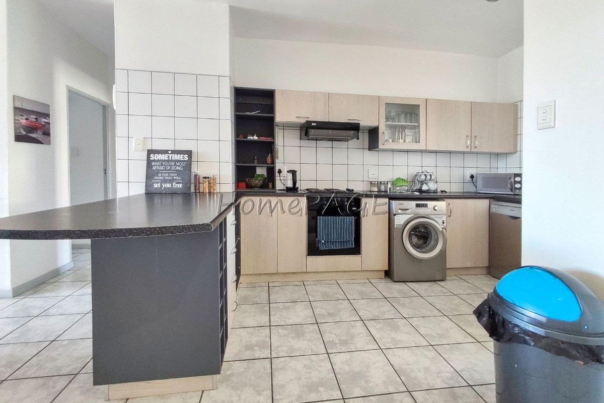 Functional kitchen featuring light wood cabinetry, dark countertops, a breakfast bar, built-in oven, hob, extractor fan, and integrated laundry plumbing.
