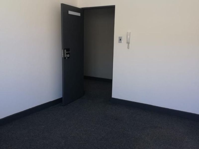 A vacant office space featuring dark carpeting, a suspended ceiling, and an intercom system, providing a clean and functional professional environment.