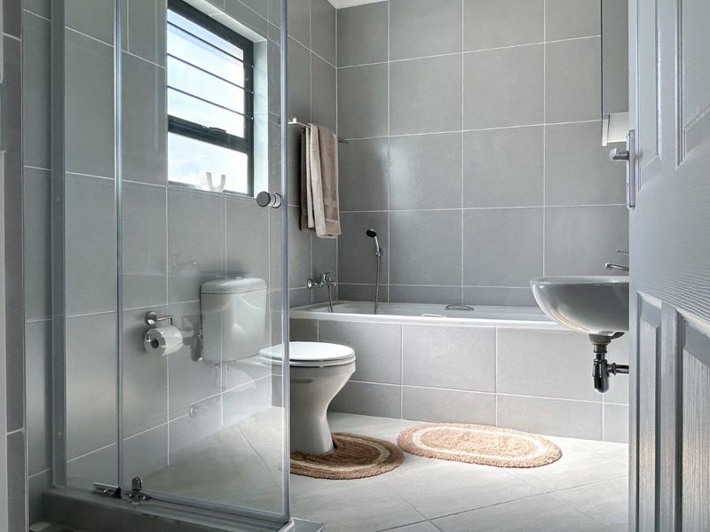 Modern bathroom featuring a glass shower enclosure, built-in bathtub, wall-mounted basin, and neutral grey floor-to-ceiling tiling.