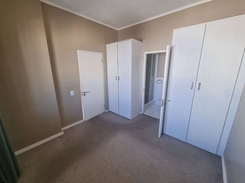 A clean, empty bedroom featuring neutral wall tones, carpeted flooring, and ample built-in cupboard storage with direct access to an en-suite bathroom.