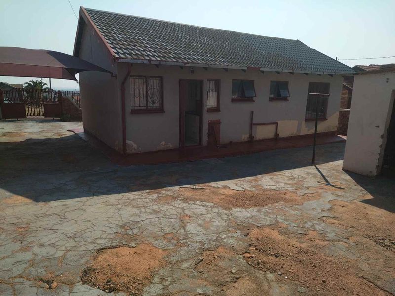 Rear view of the property featuring a tiled roof, security bars on windows, and a large concrete driveway area in need of maintenance.