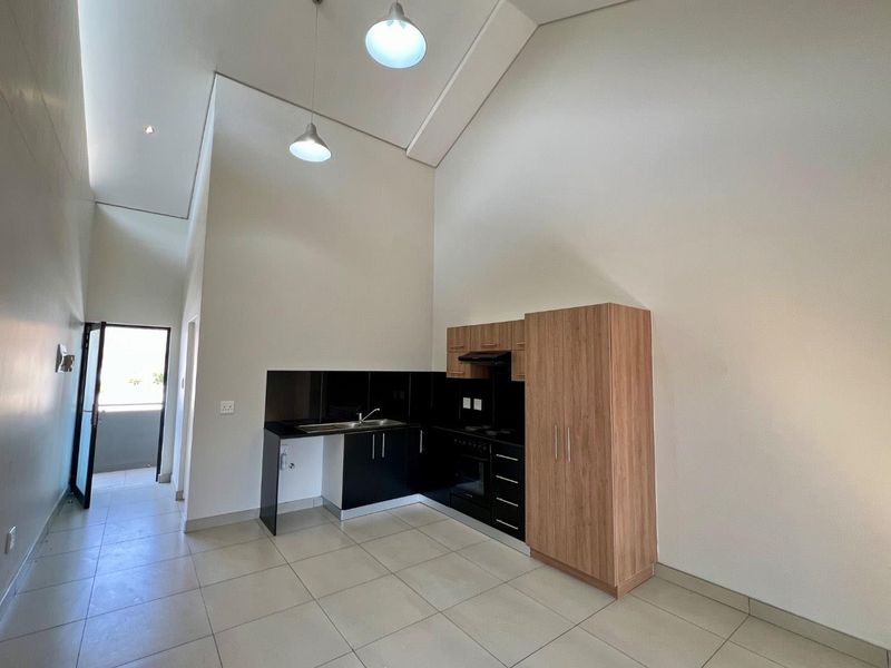 Modern kitchen area featuring high ceilings, built-in cabinetry, integrated oven, extractor fan, and tiled flooring in an open-plan layout.